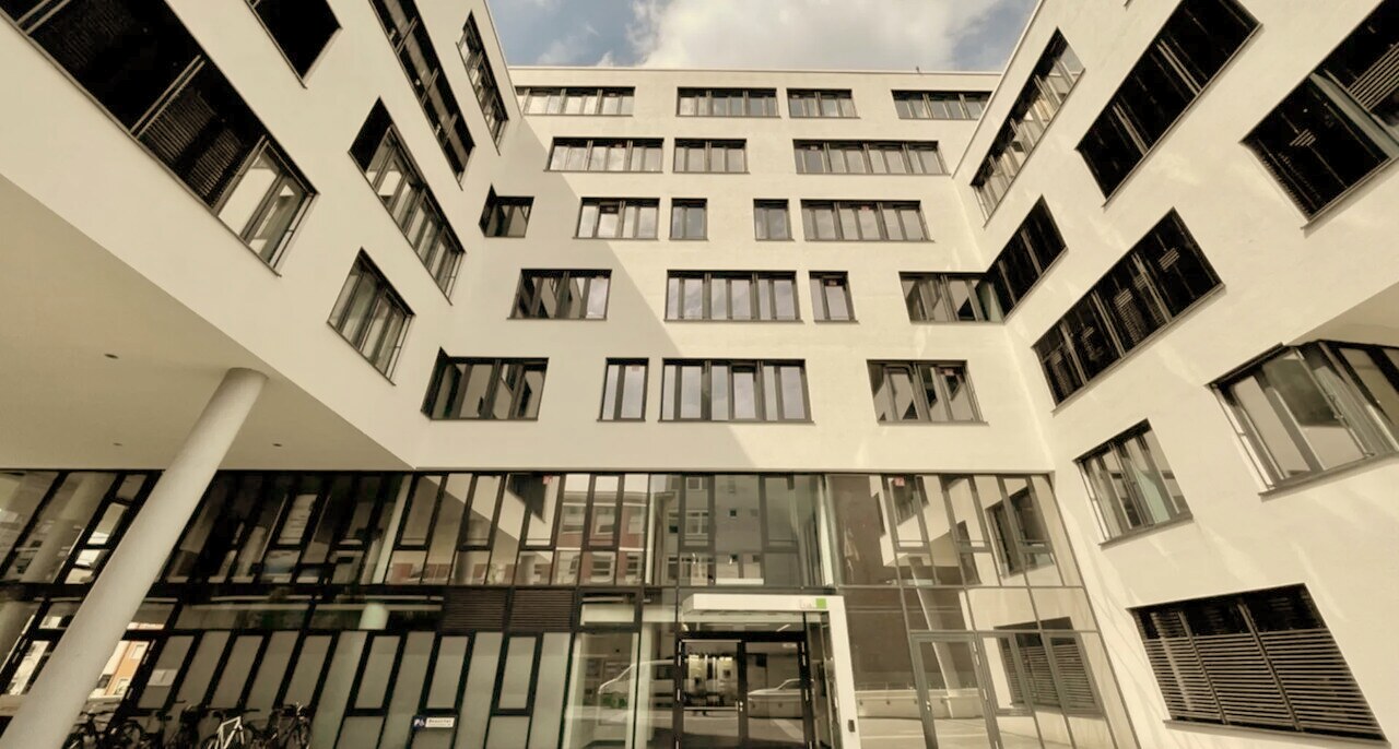 Heller moderner Innenhof eines weißen Bürogebäudes der PMD. Group mit großflächigen Fensterfronten
