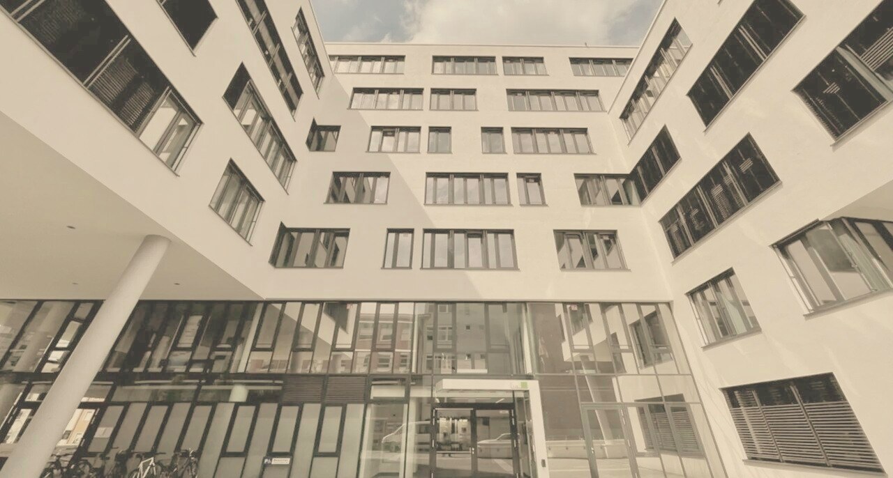 Heller moderner Innenhof eines weißen Bürogebäudes mit großflächigen Fensterfronten